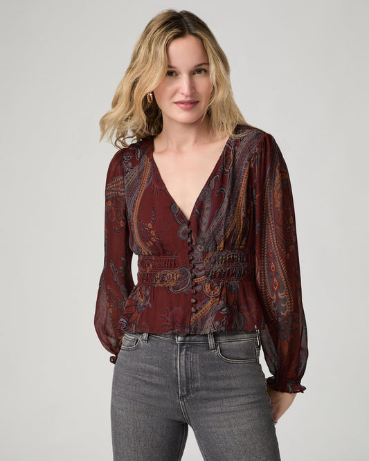 Close-up front view of a woman wearing the garnet paisley-print Juna Blouse with a V-neckline and smocked waist, paired with gray jeans.