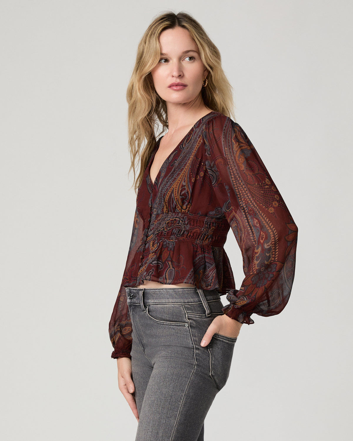 Close-up front view of a woman wearing the garnet paisley-print Juna Blouse, adjusting the gathered cuff at her wrist.