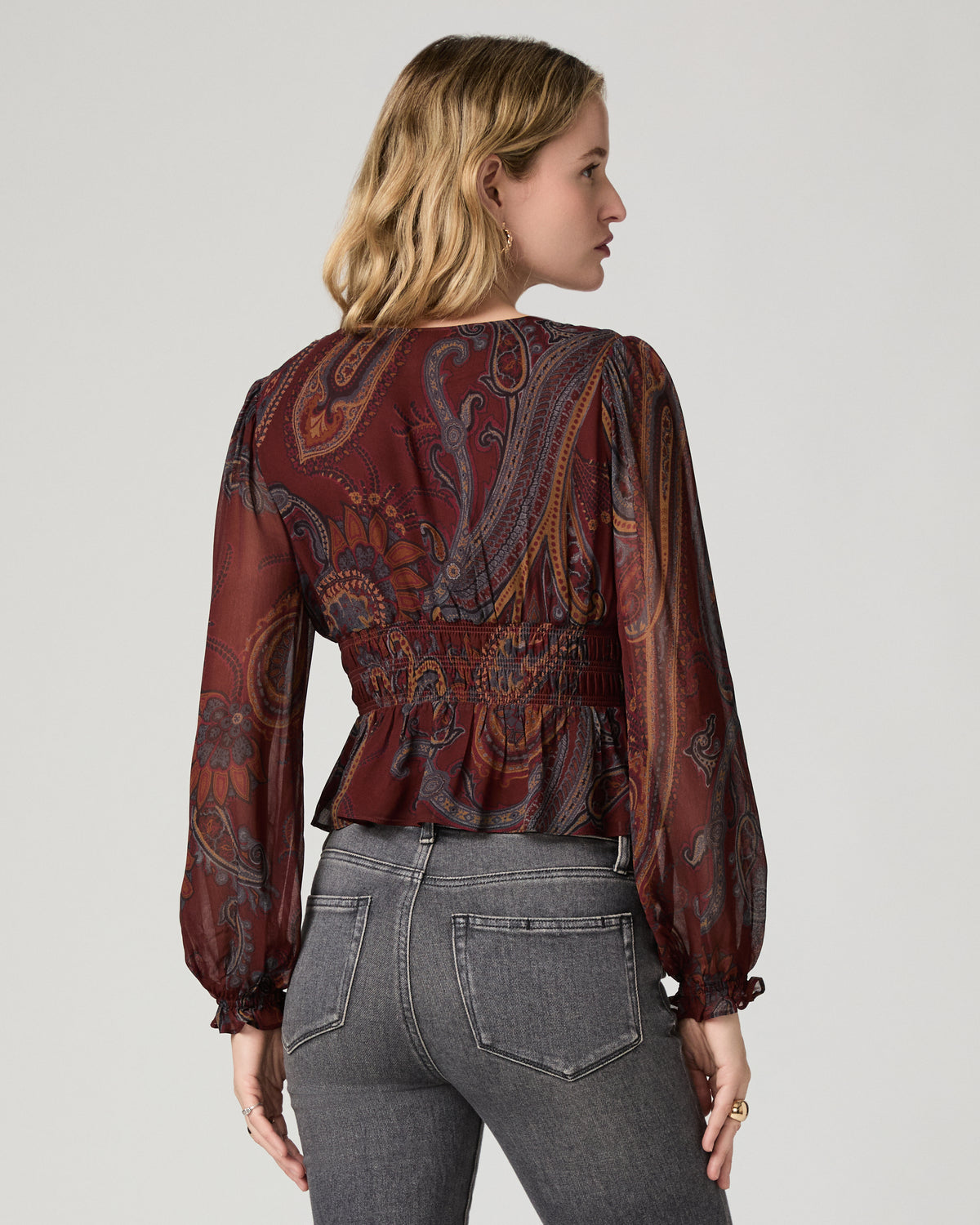 Back view of a woman wearing the garnet paisley-print Juna Blouse, showing the smocked detailing at the waist.