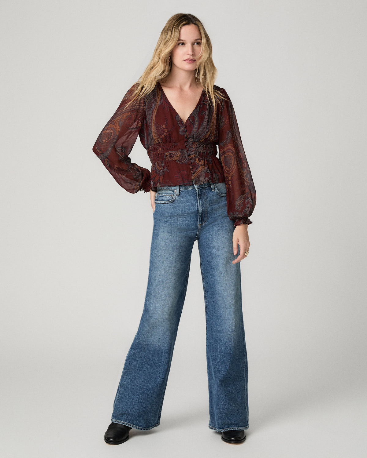 Front view of a woman wearing the garnet paisley-print Juna Blouse tucked into light-wash flared jeans.