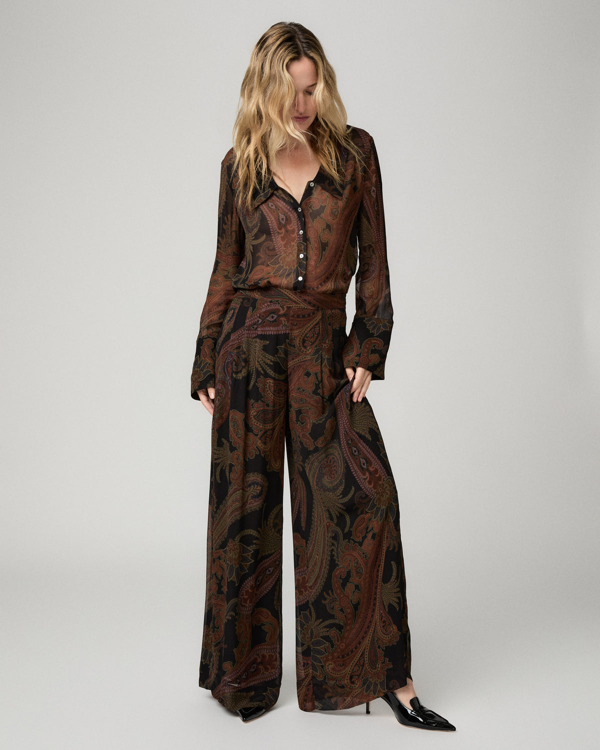 Full-length front view of a woman wearing the black and brown paisley-print Carina Pant with a matching paisley blouse and black heels.