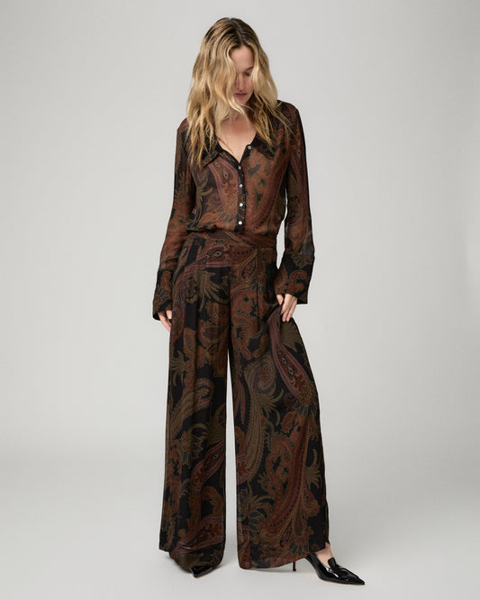Full-length front view of a woman wearing the black and brown paisley-print Carina Pant with a matching paisley blouse and black heels.