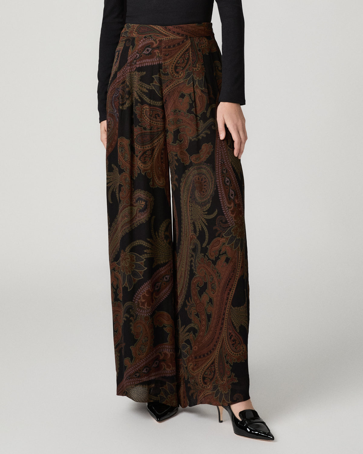 Close-up of a woman wearing the black and brown paisley-print Carina Pant with a black fitted top, paired with black pointed shoes.