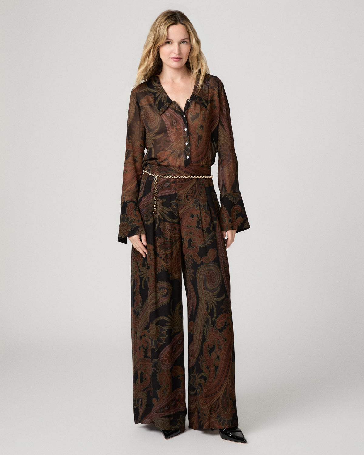 Full-length front view of a woman wearing the black and brown paisley-print Carina Pant with a matching paisley blouse and smocked waistband belt.