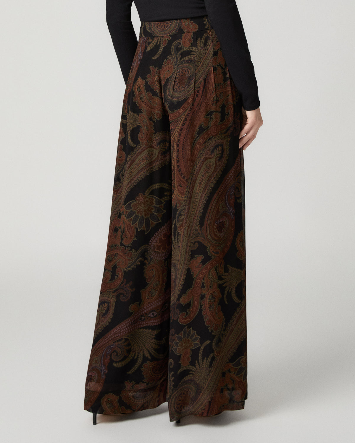 Close-up of the black and brown paisley-print Carina Pant's wide-leg silhouette and high-rise waistband, paired with a black fitted top.