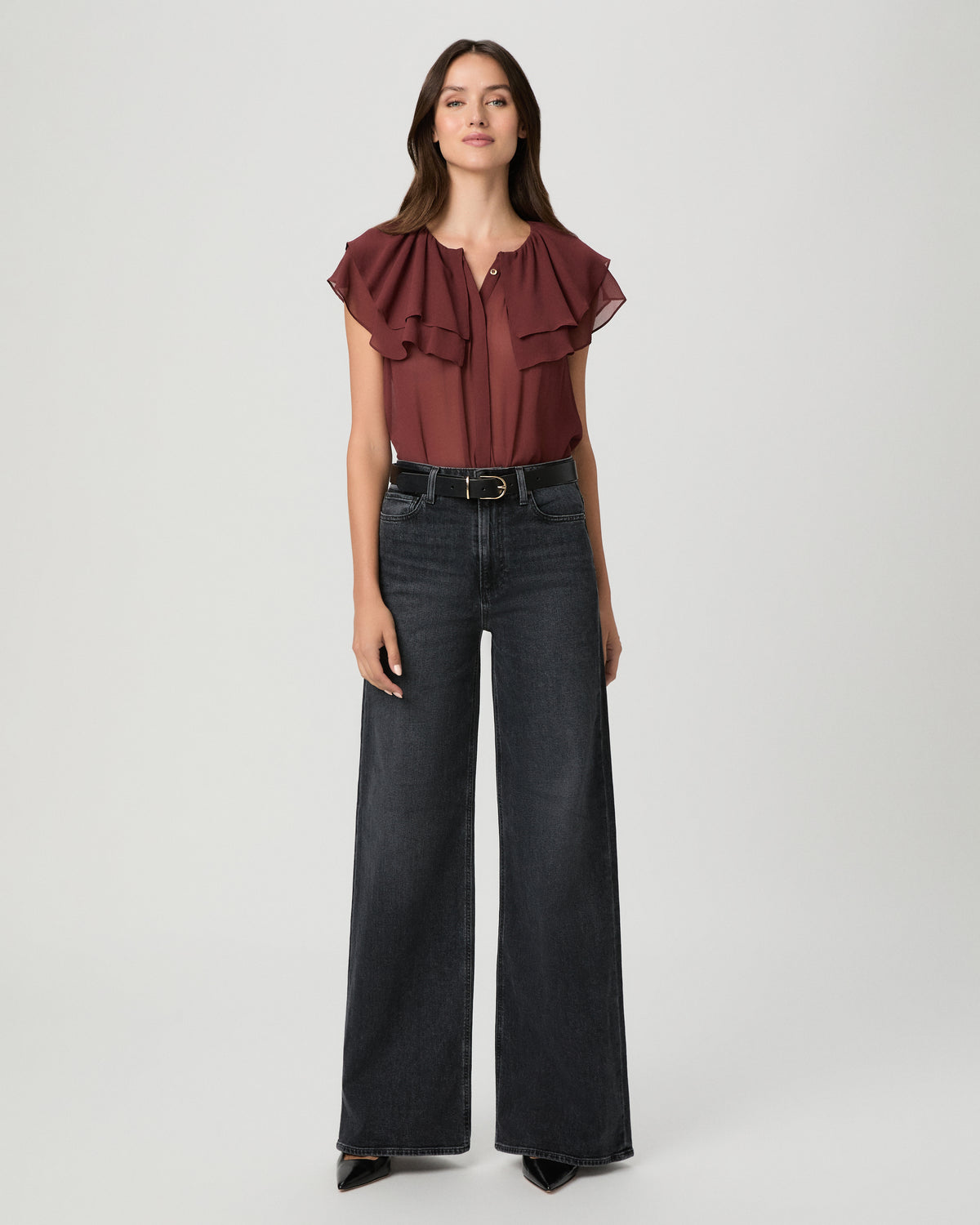 A woman modeling a brown short-sleeve top and black wide-leg pants against a light gray studio background.