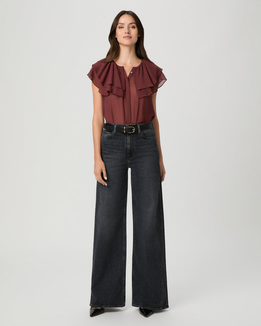 A woman modeling a brown short-sleeve top and black wide-leg pants against a light gray studio background.