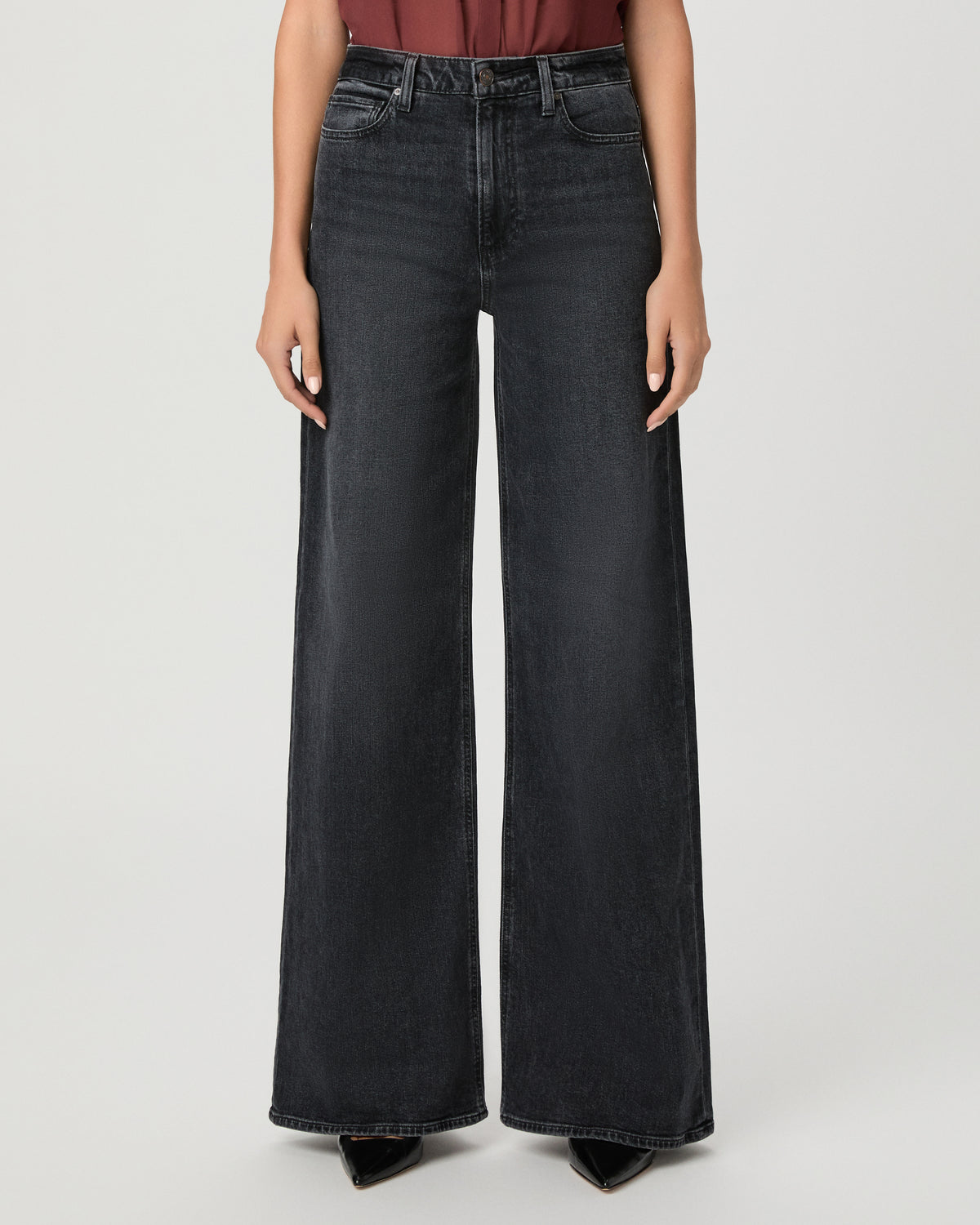 A woman modeling a brown short-sleeve top and black wide-leg pants against a light gray studio background.