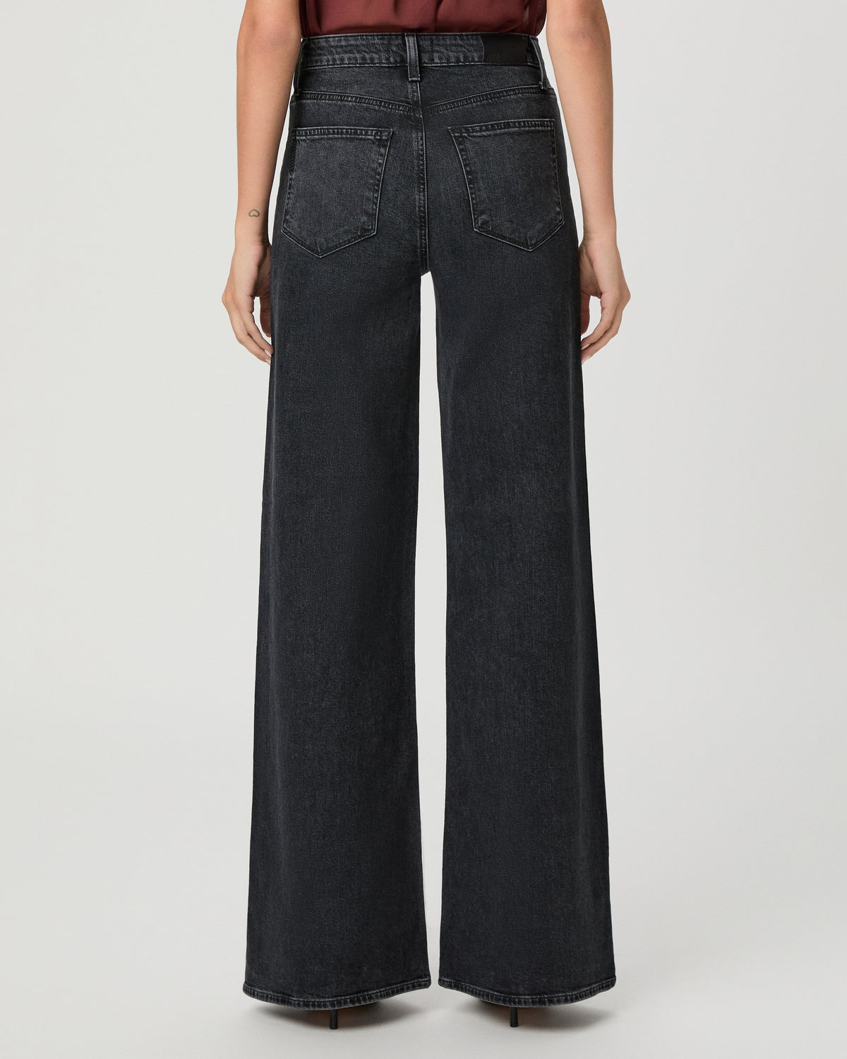 A woman modeling a brown short-sleeve top and black wide-leg pants against a light gray studio background.