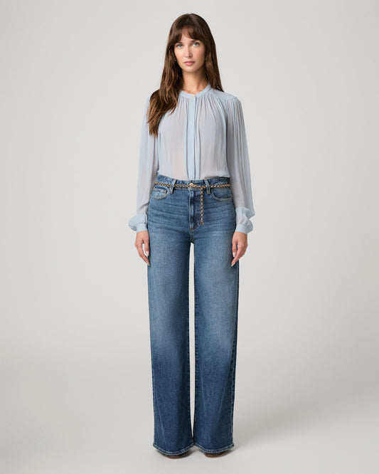 Woman wearing a light blue top and blue pants against a white background