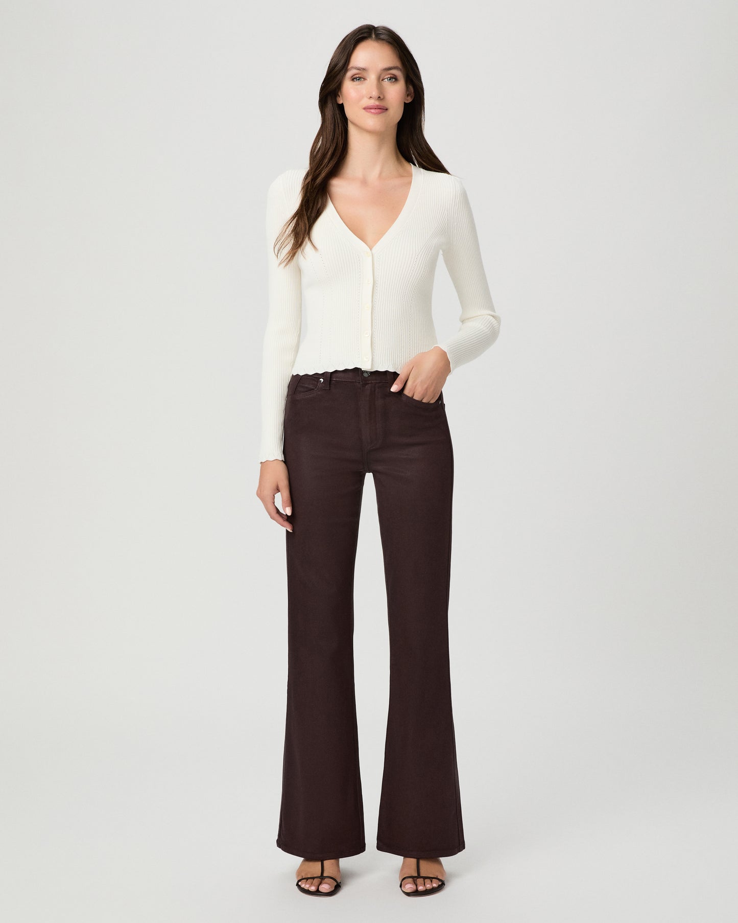 A woman modeling a cream long-sleeve knit cardigan with a V-neck and button front, paired with dark brown wide-leg pants, against a light gray studio background.