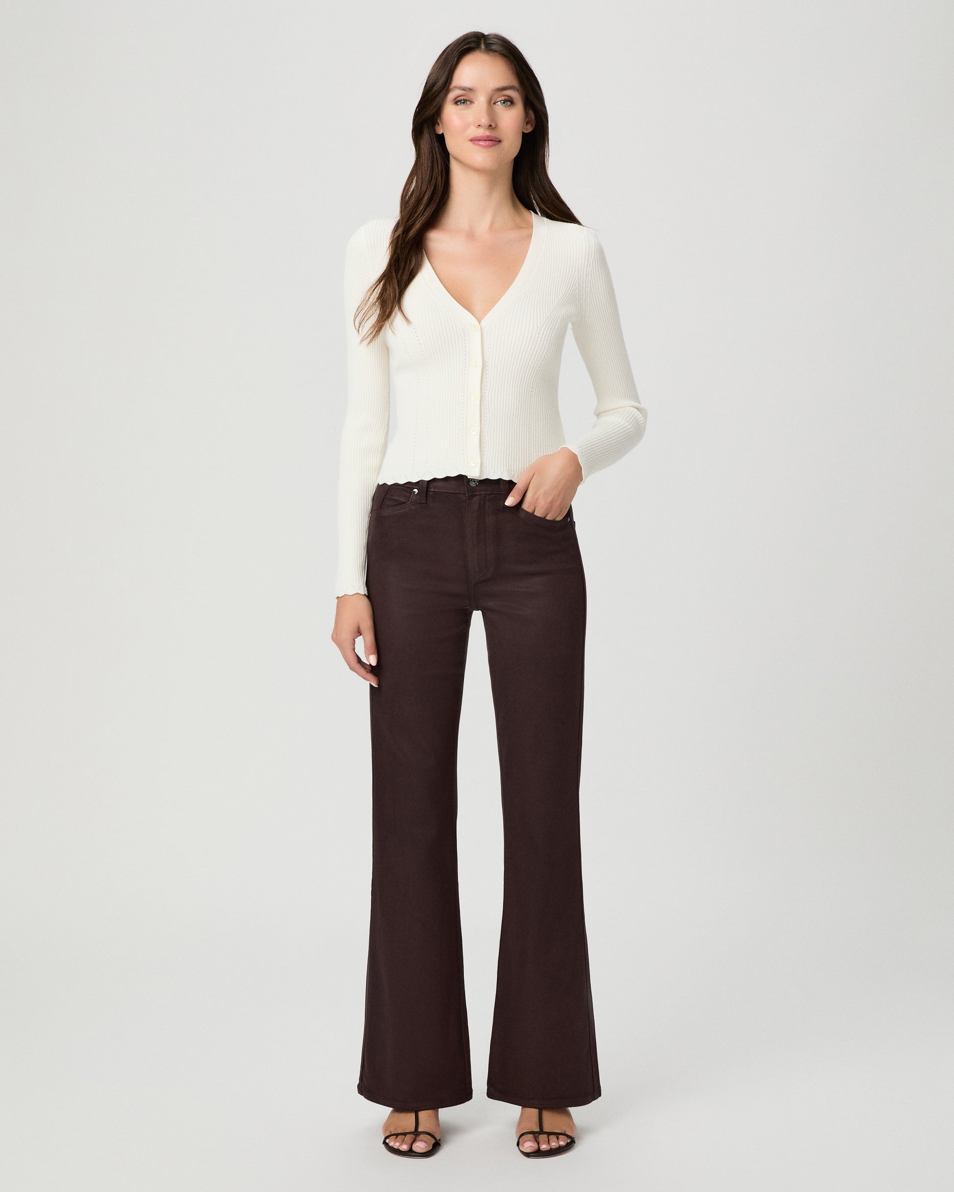 A woman modeling a cream long-sleeve knit cardigan with a V-neck and button front, paired with dark brown wide-leg pants, against a light gray studio background.