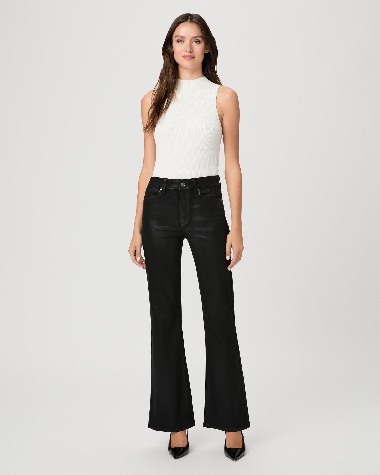 A woman modeling a sleeveless white mock-neck top and black wide-leg flare jeans against a light gray studio background.