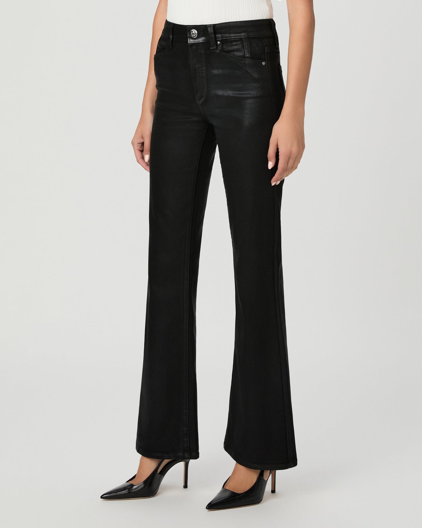 A woman modeling a sleeveless white mock-neck top and black wide-leg flare jeans against a light gray studio background.