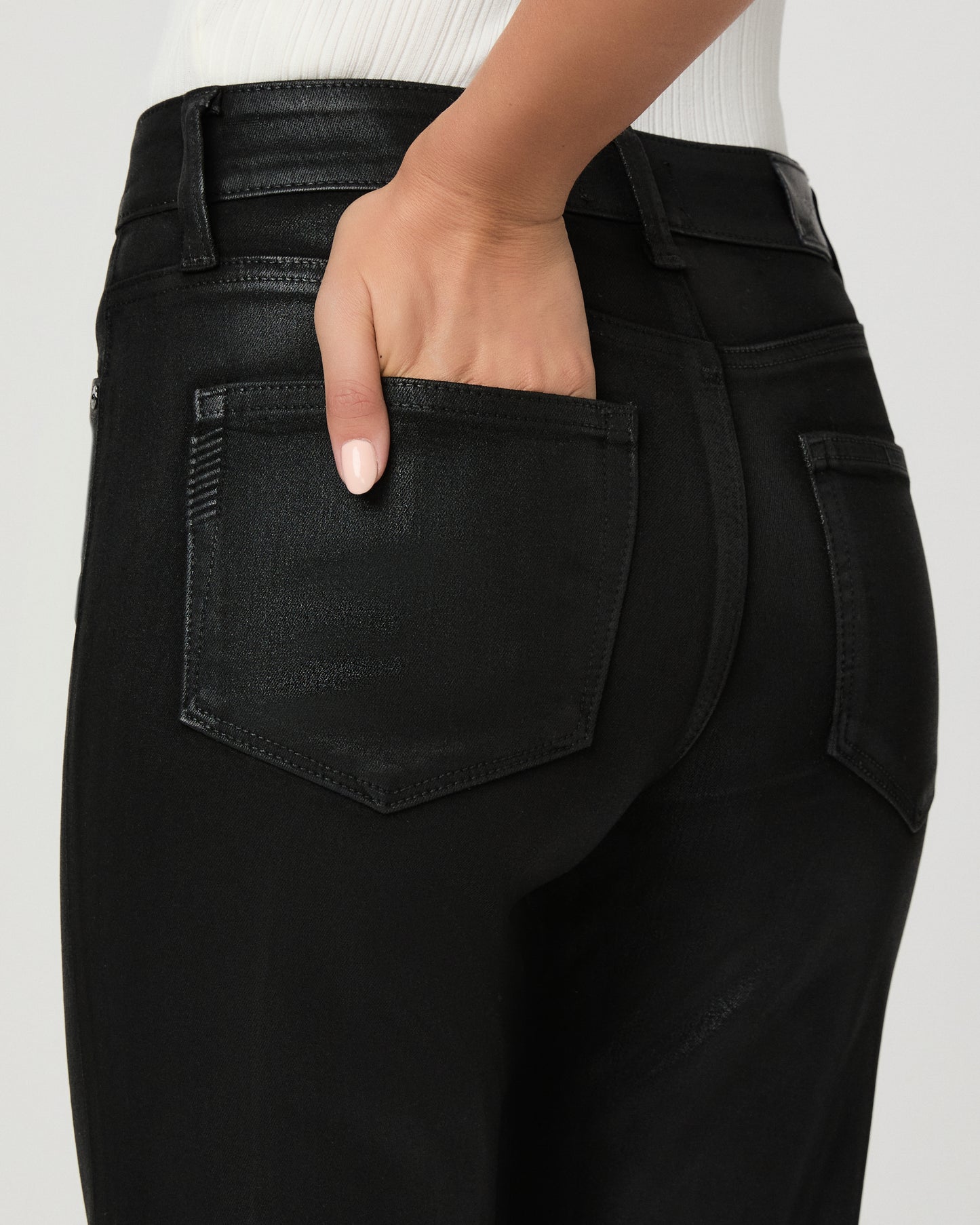 A woman modeling a sleeveless white mock-neck top and black wide-leg flare jeans against a light gray studio background.