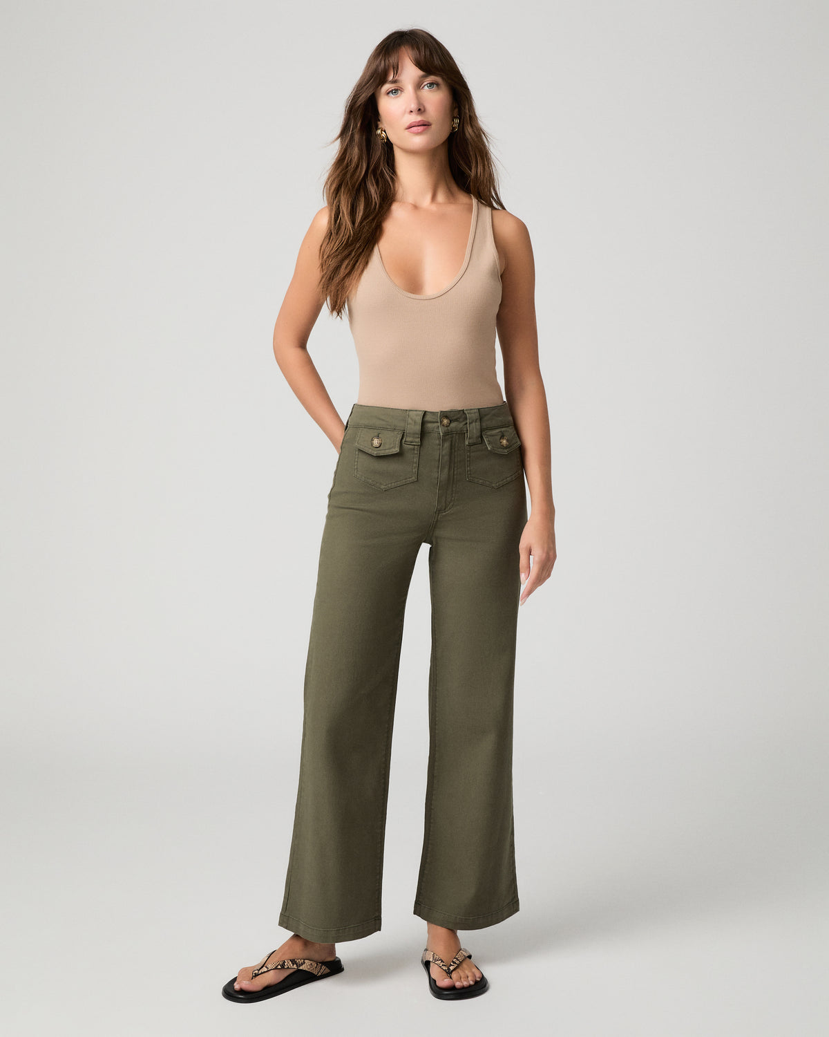 Woman wearing nude top and green pants against a white background