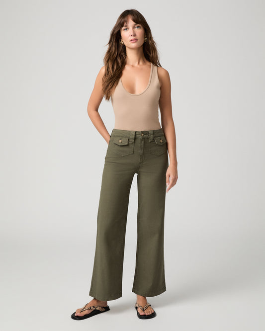 Woman wearing nude top and green pants against a white background