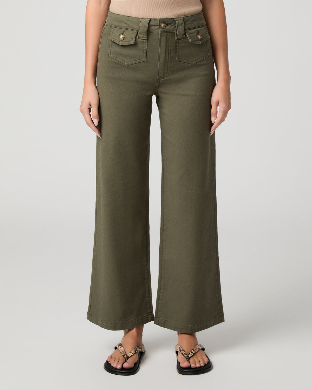Woman wearing nude top and green pants against a white background