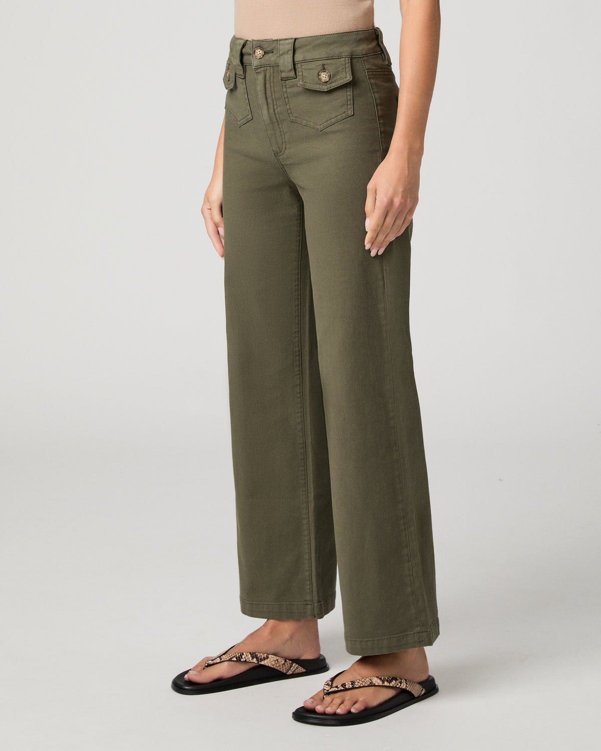Woman wearing nude top and green pants against a white background