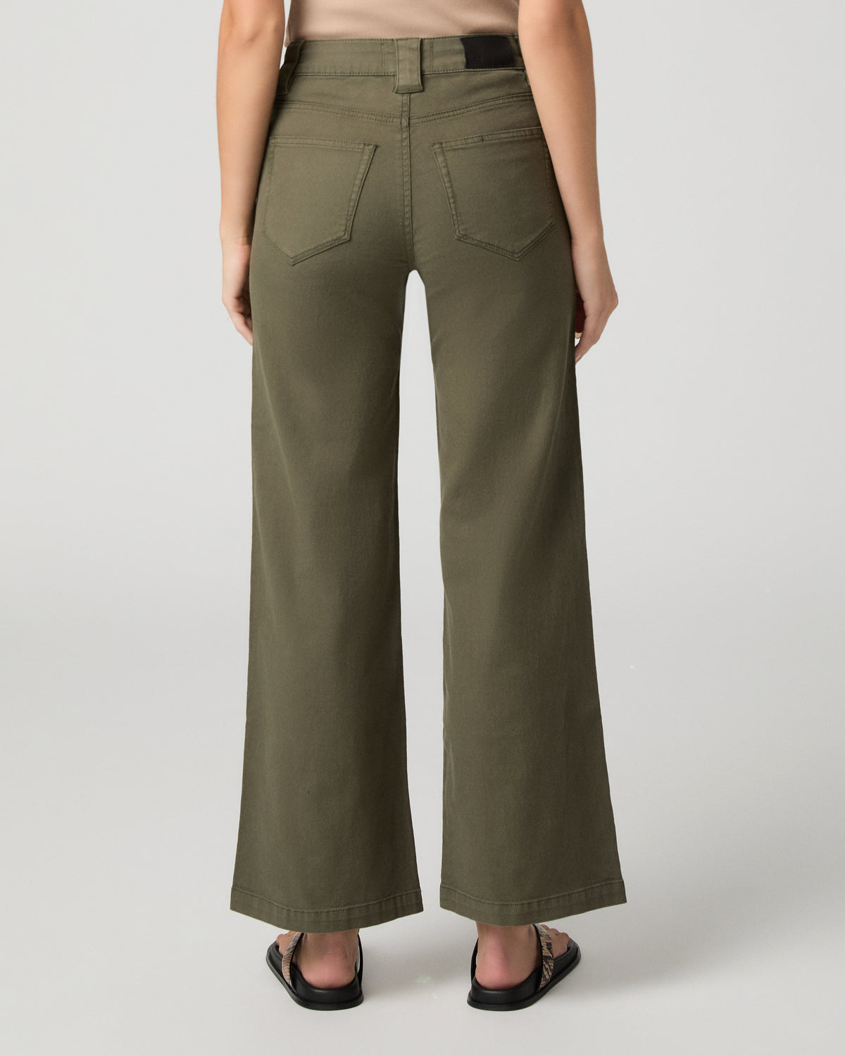 Woman wearing nude top and green pants against a white background