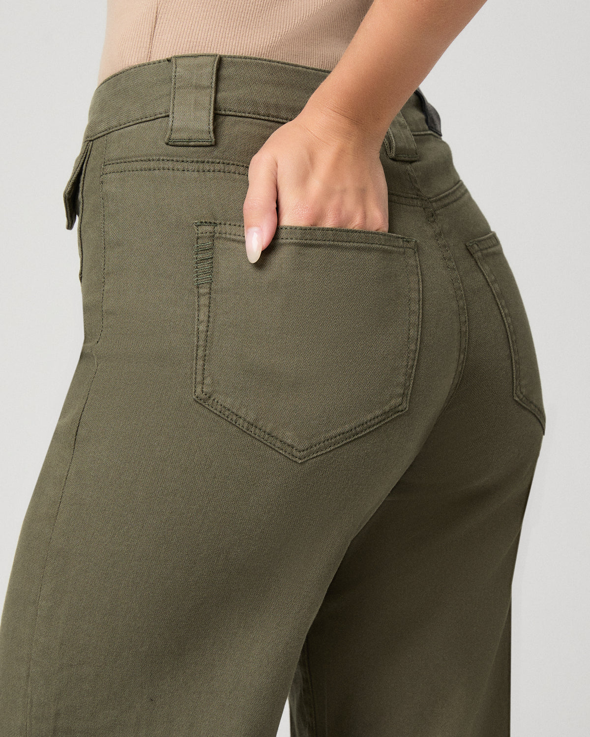 Woman wearing nude top and green pants against a white background