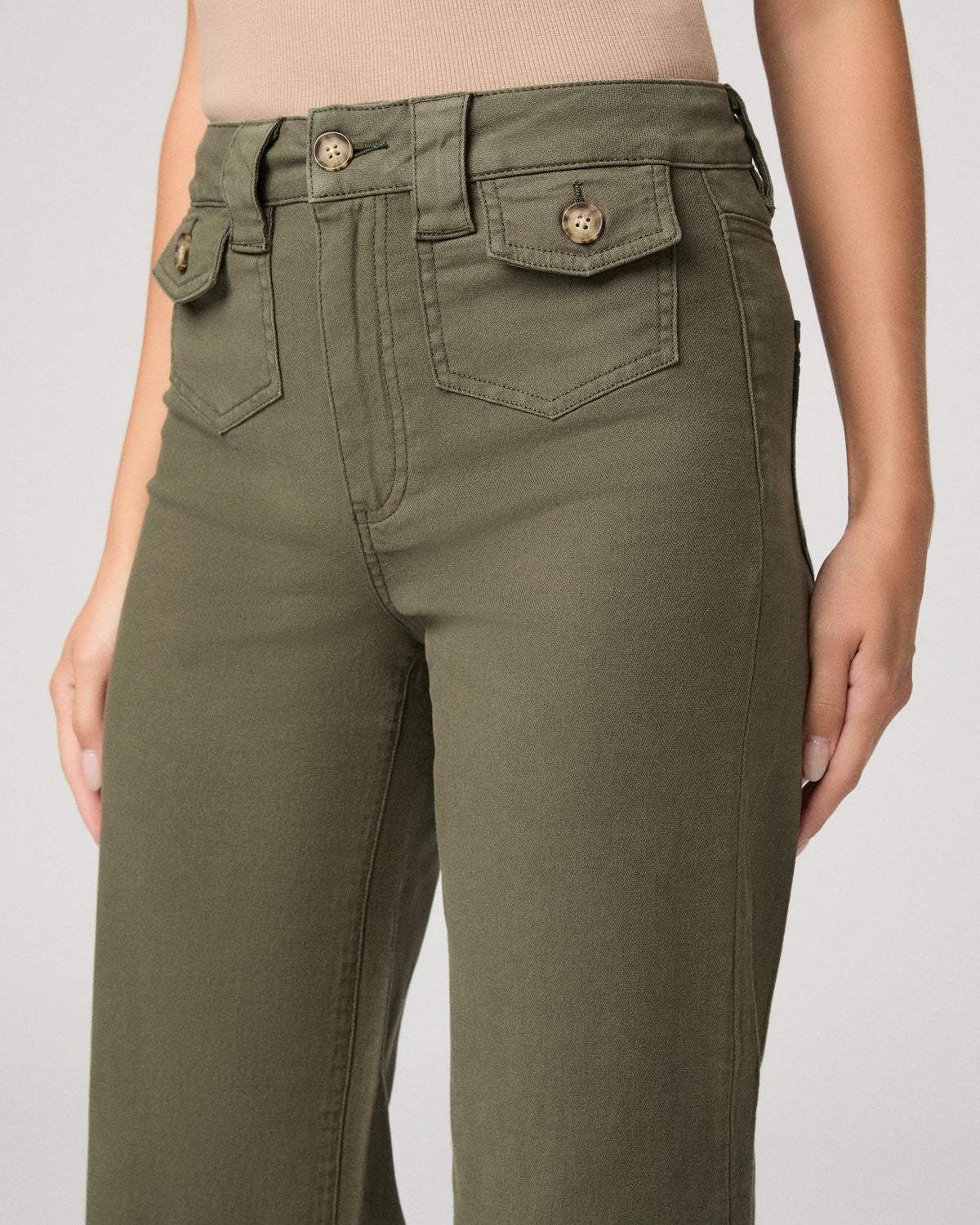 Woman wearing nude top and green pants against a white background