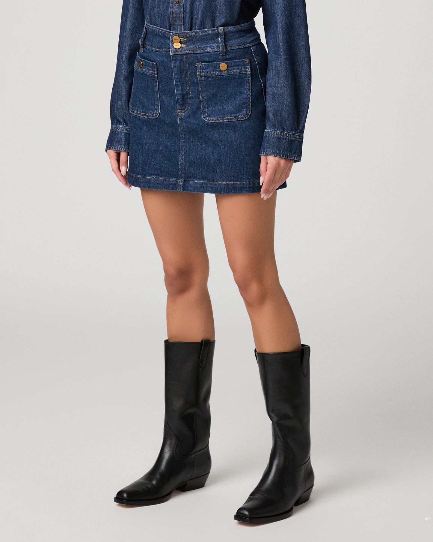 Woman wearing blue top, blue skirt and black boots against a white background