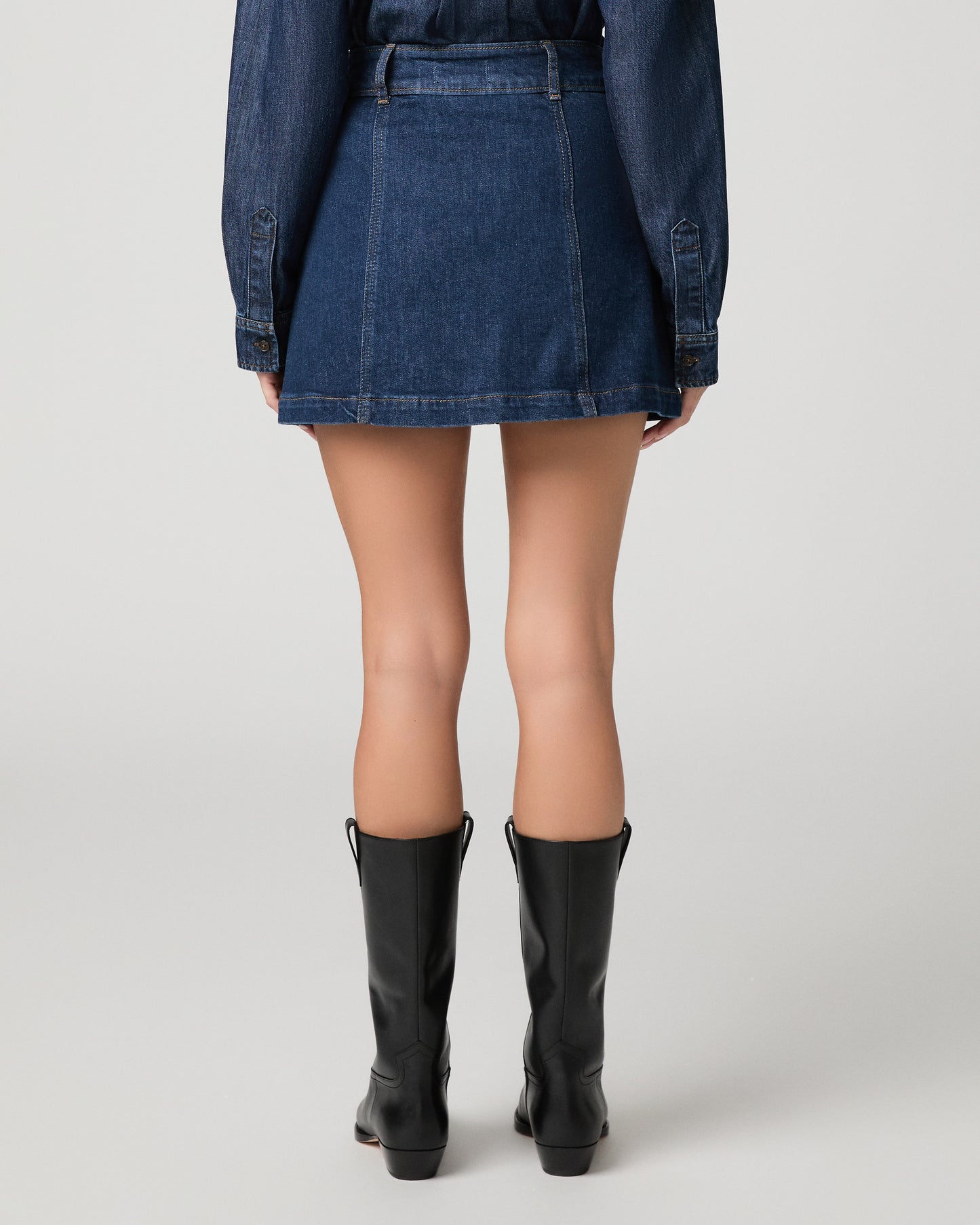 Woman wearing blue top, blue skirt and black boots against a white background