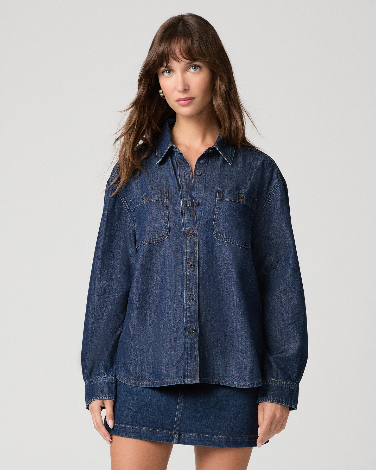 Woman wearing a dark denim top paired with dark denim skirt against a white background
