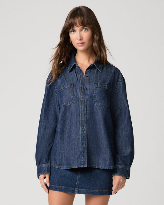 Woman wearing a dark denim top paired with dark denim skirt against a white background