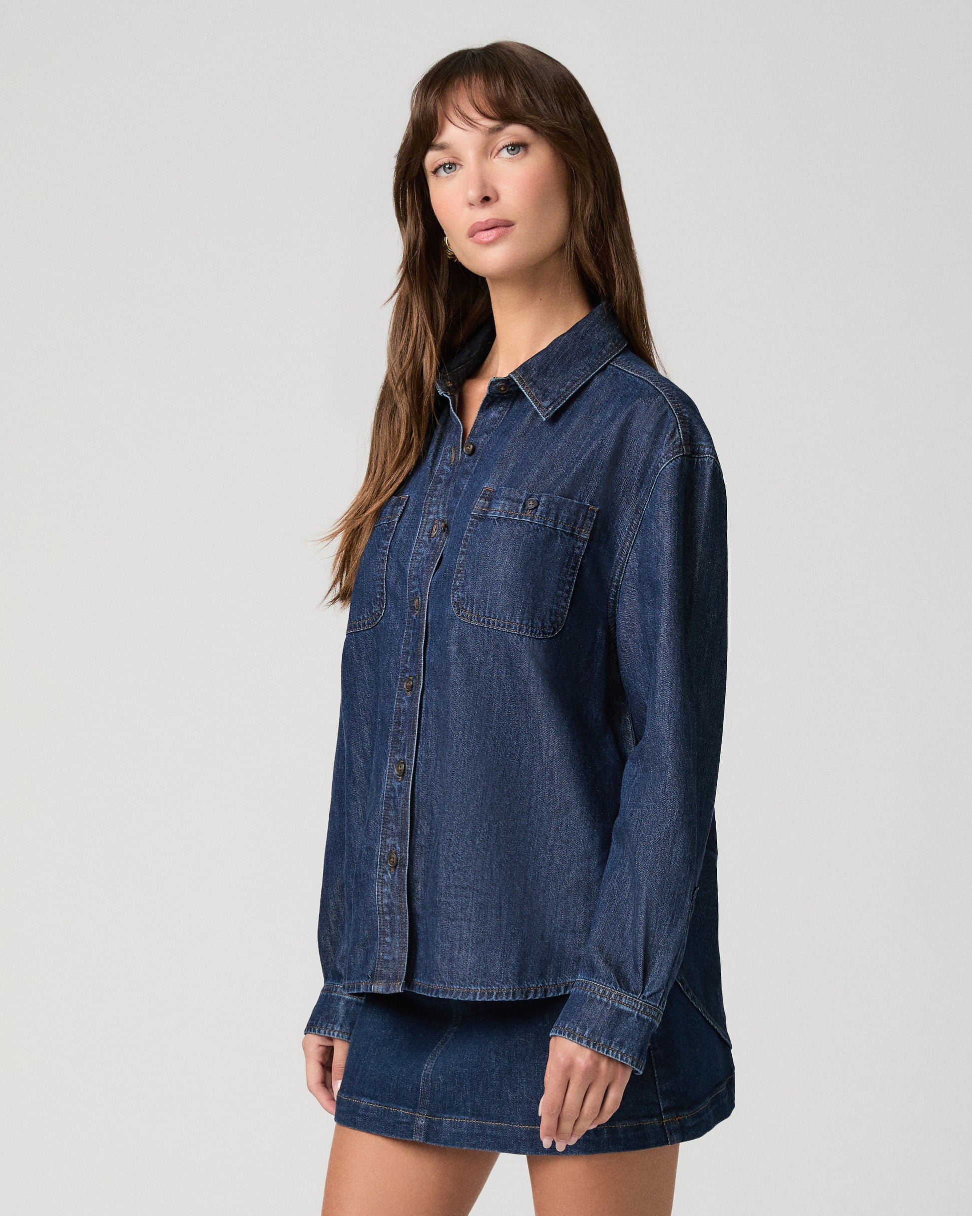 Woman wearing a dark denim top paired with dark denim skirt against a white background