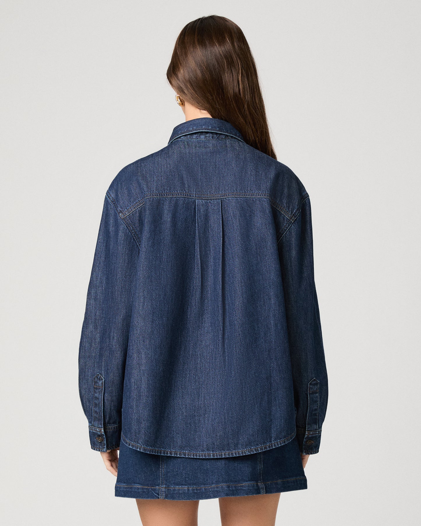 Woman wearing a dark denim top paired with dark denim skirt against a white background