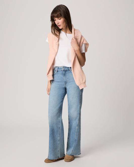 Woman wearing a light pink cardigan, white top, and blue jeans on a plain background