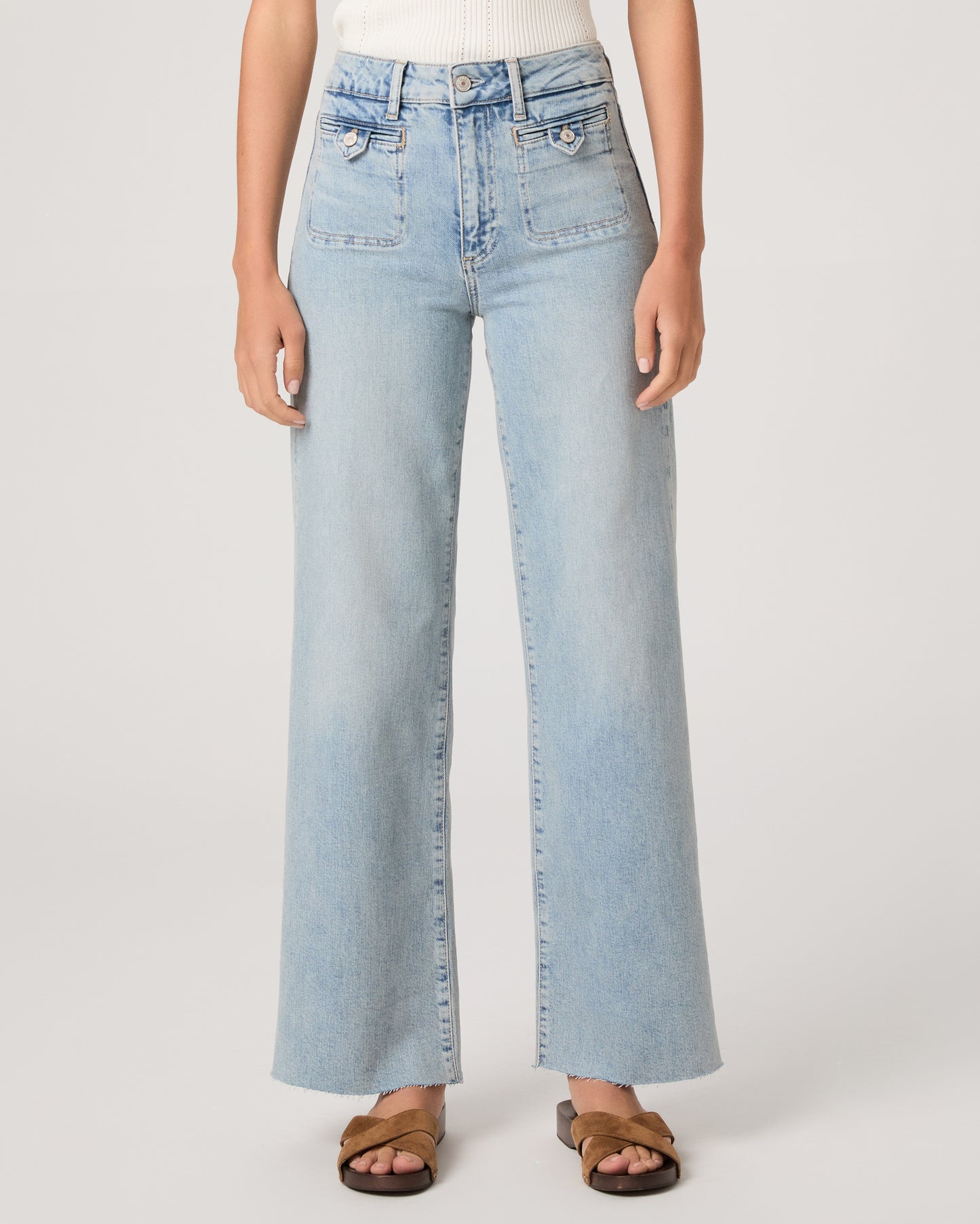 Model wearing a white tub top paired with light wash jeans and brown sandals against a white background. 