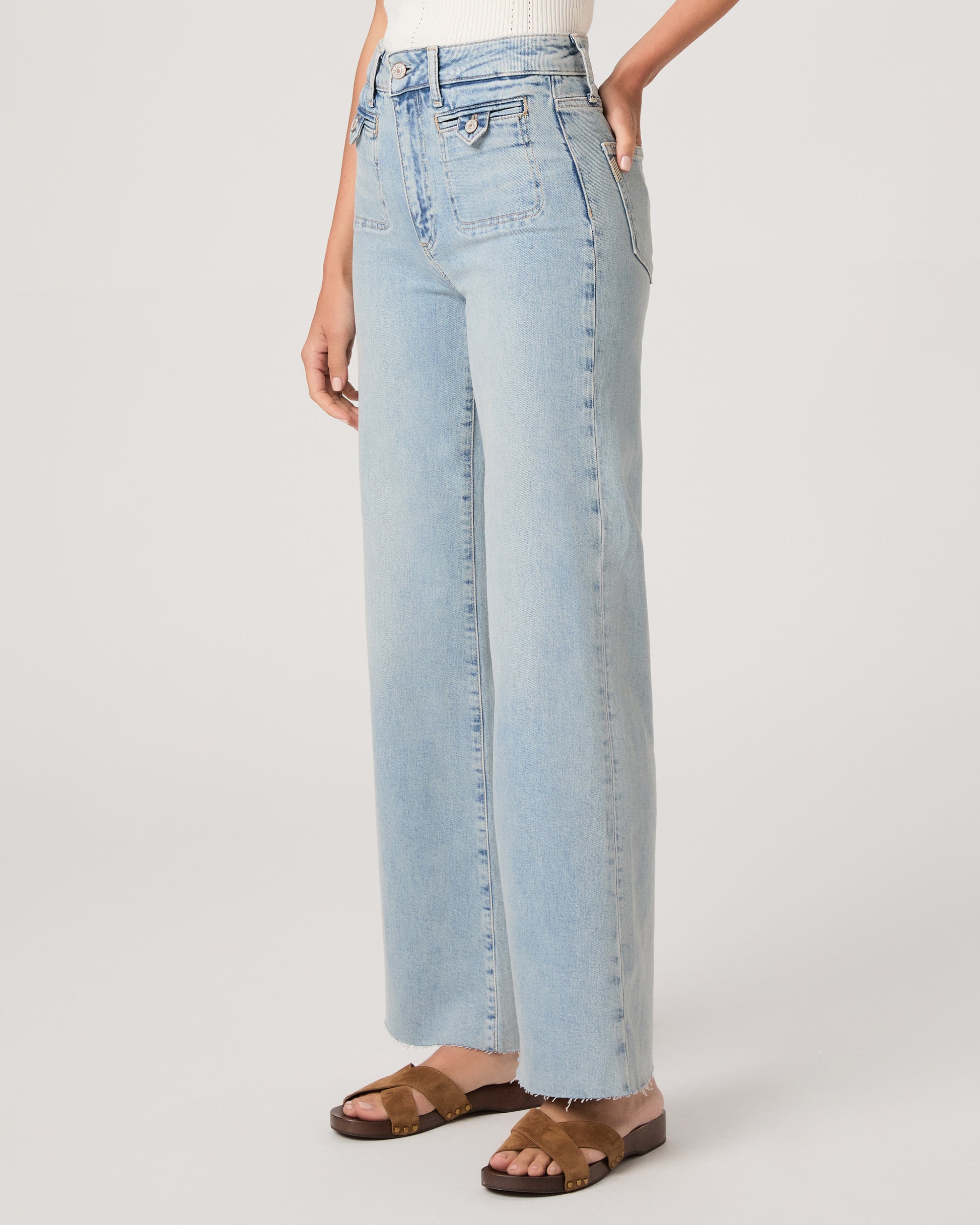 Model wearing a white tub top paired with light wash jeans and brown sandals against a white background. 