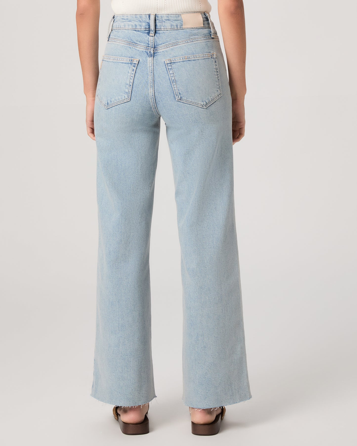 Model wearing a white tub top paired with light wash jeans and brown sandals against a white background. 