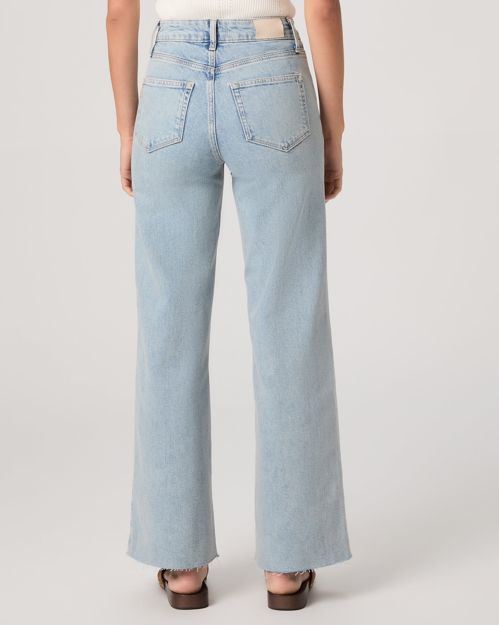 Model wearing a white tub top paired with light wash jeans and brown sandals against a white background. 