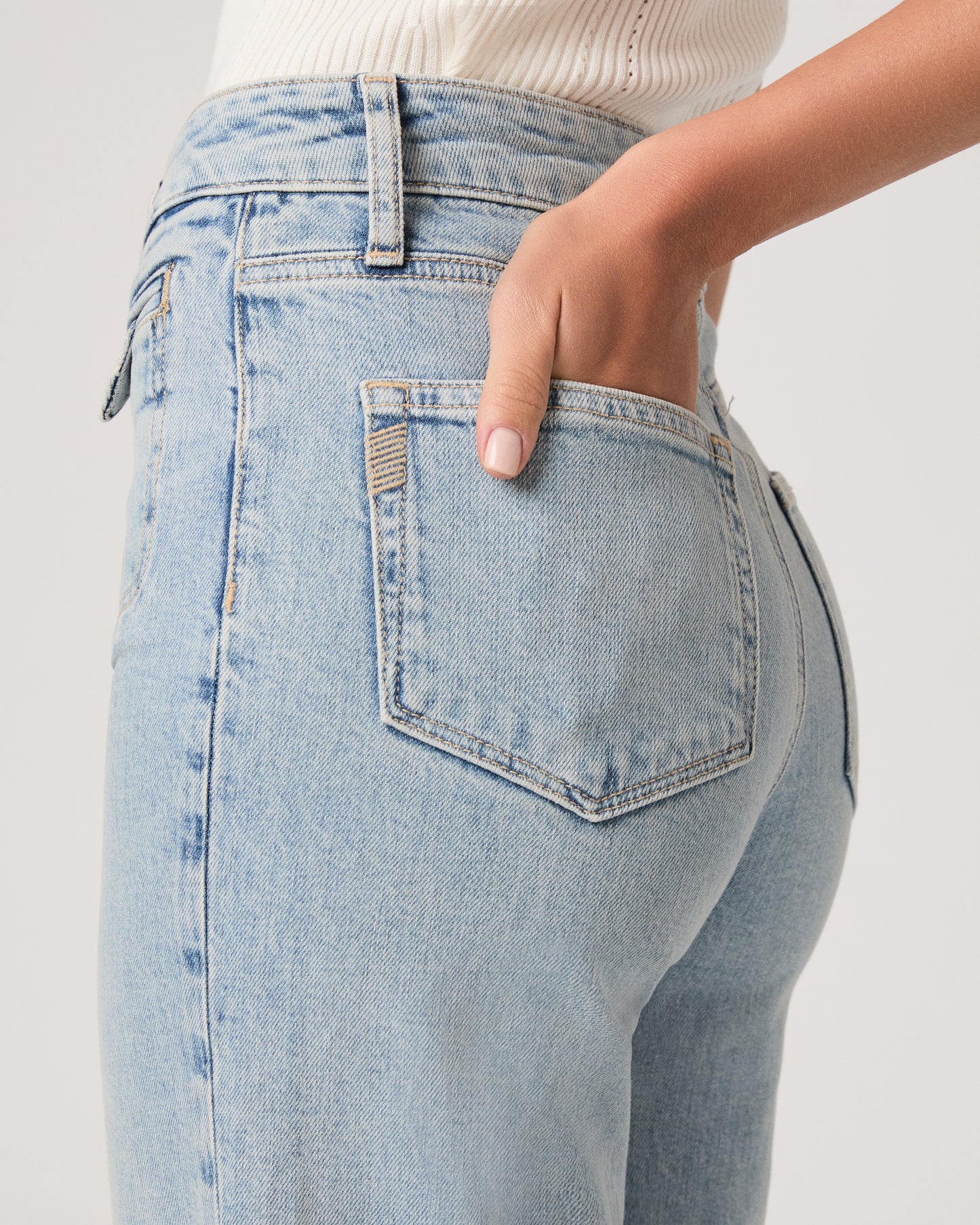 Model wearing a white tub top paired with light wash jeans and brown sandals against a white background. 
