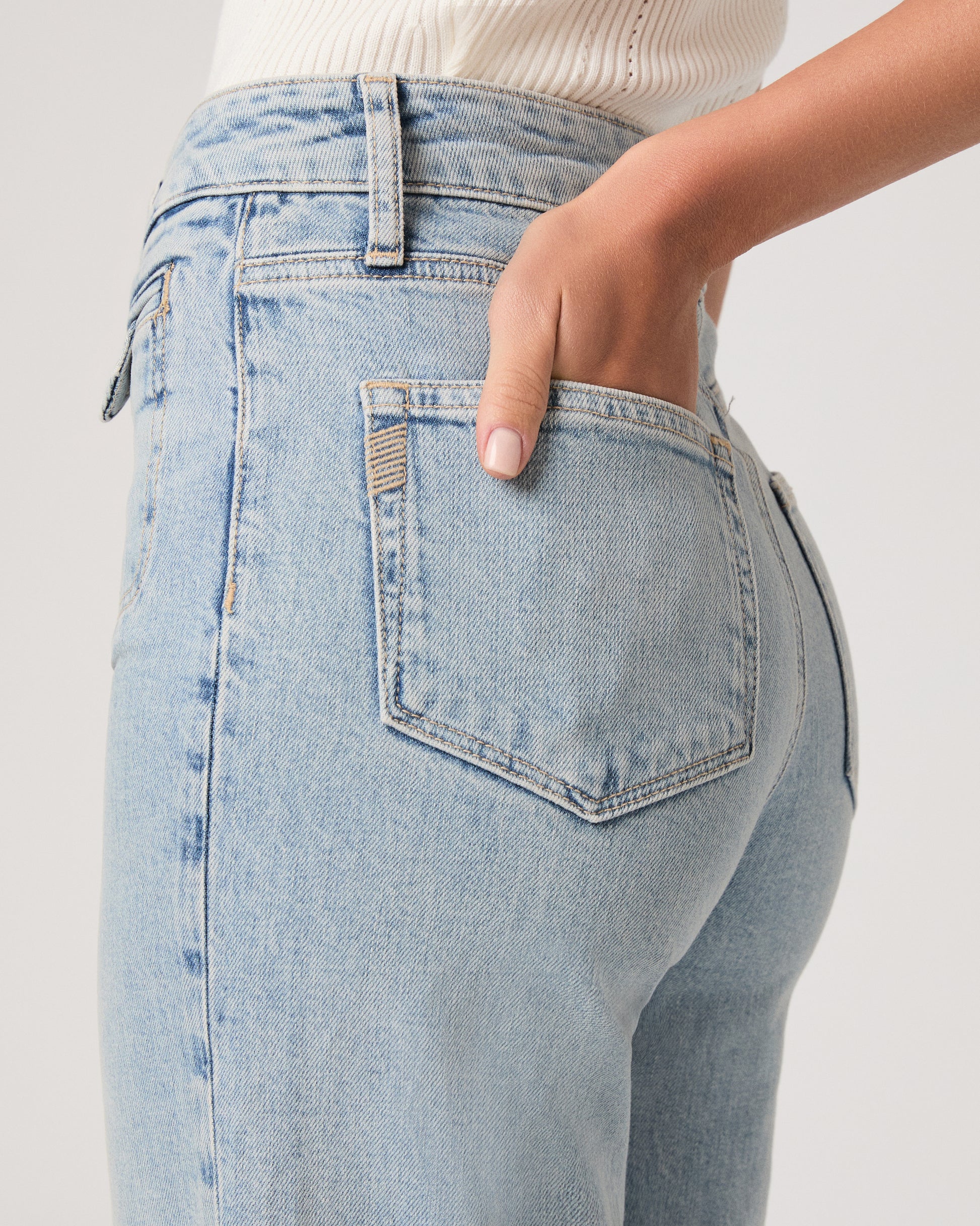 Model wearing a white tub top paired with light wash jeans and brown sandals against a white background. 