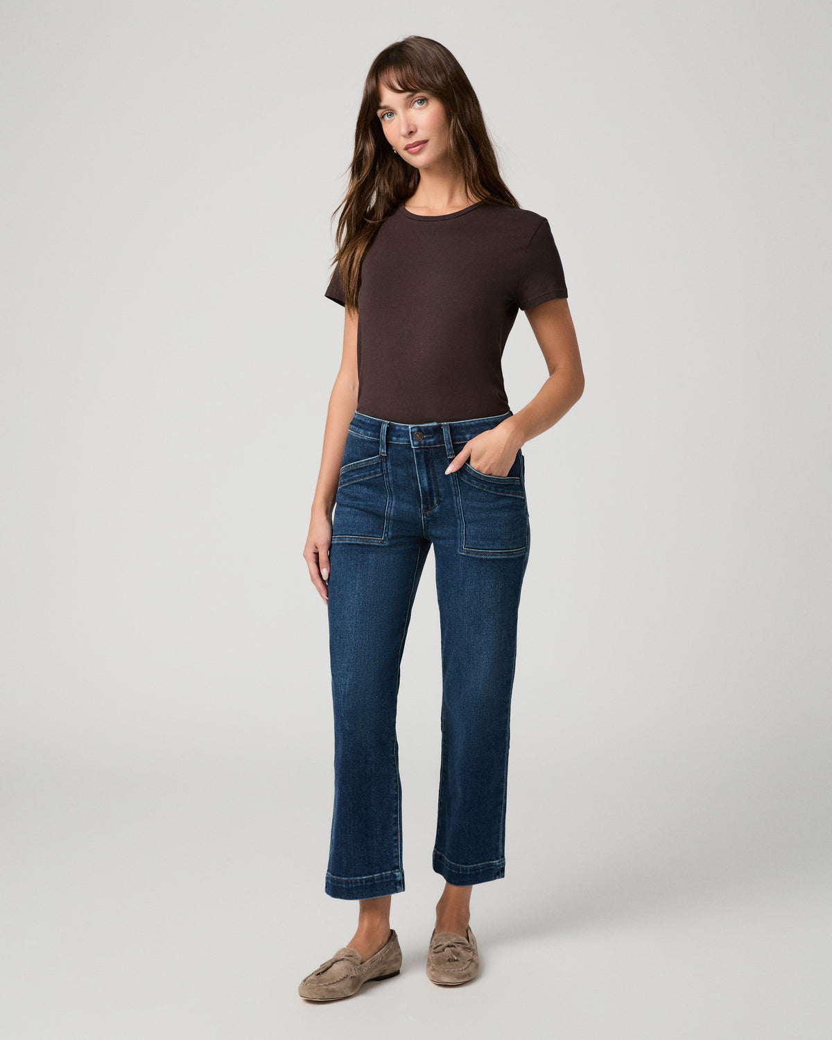 Woman wearing a brown top paired with  dark pants against a white background
