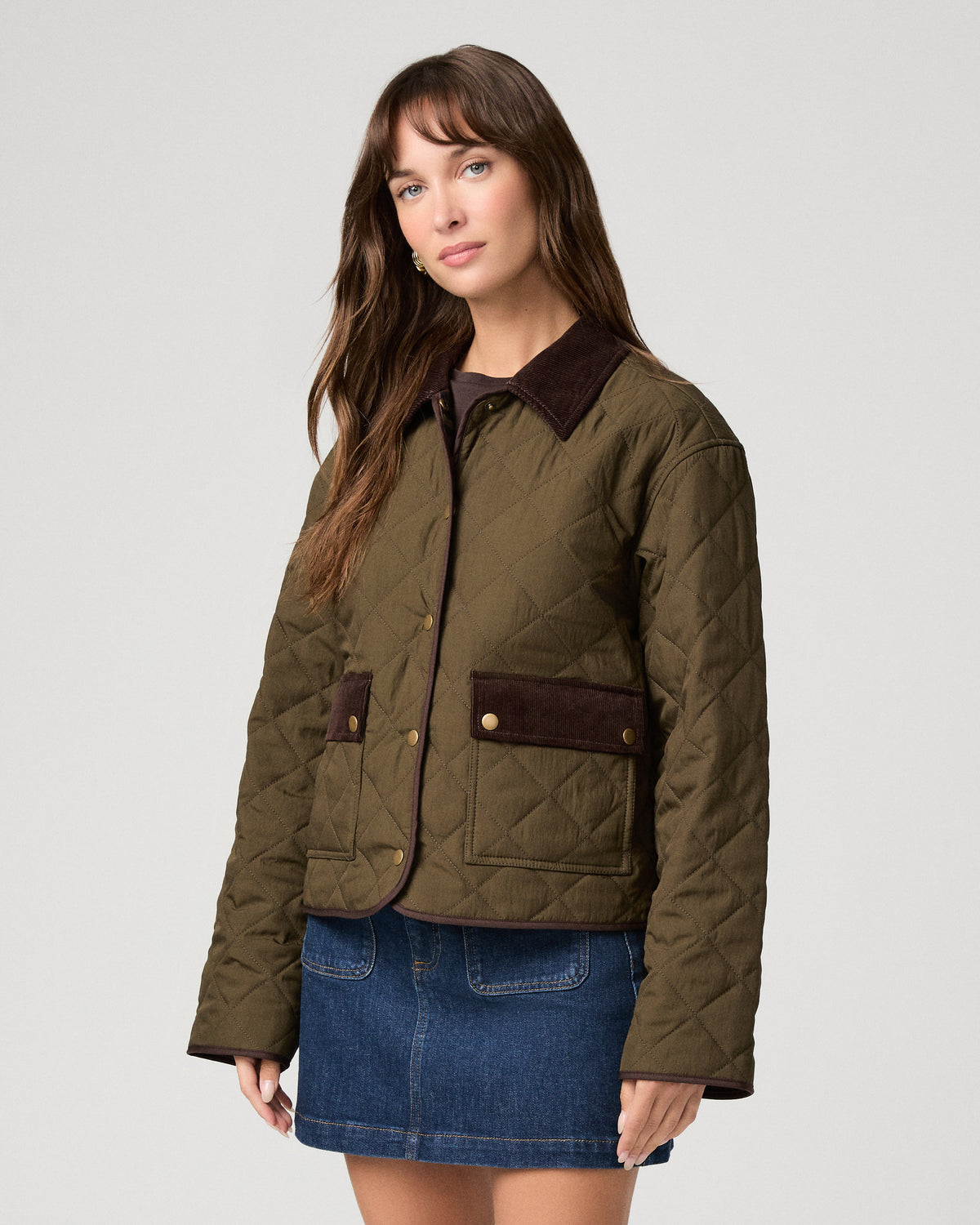 Woman wearing a green jacket and denim skirt against a white background