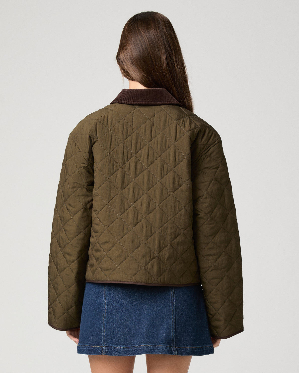Woman wearing a green jacket and denim skirt against a white background