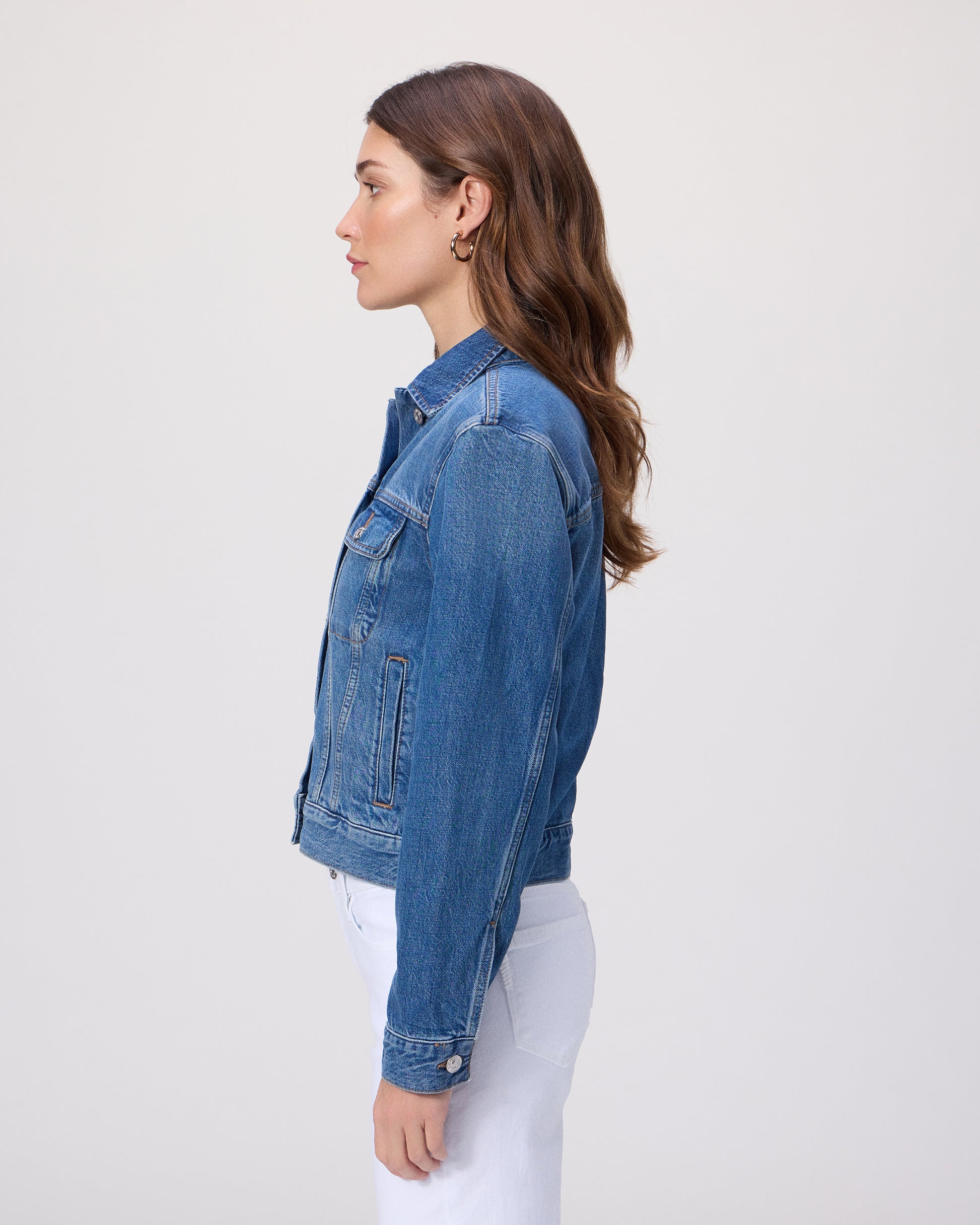 Woman wearing a blue denim jacket over a white shirt paired with white denim on a light gray background