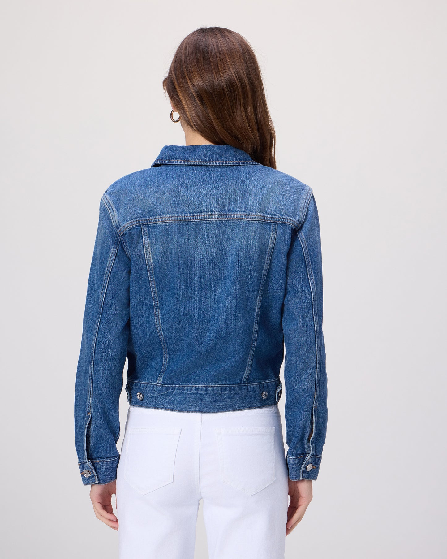 Woman wearing a blue denim jacket over a white shirt paired with white denim on a light gray background