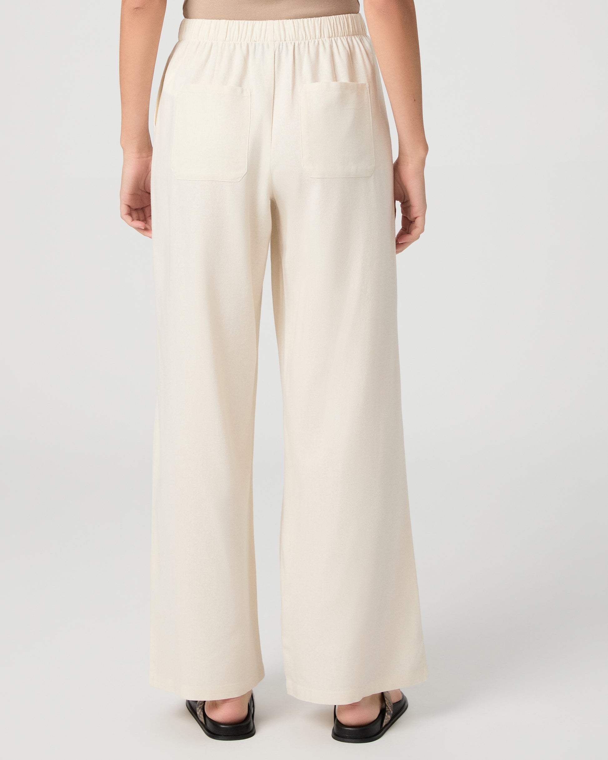 Woman wearing a beige tank top and white pants on a plain background