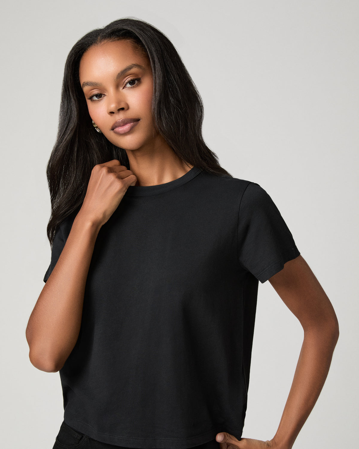 Close-up portrait of a woman wearing a black crew-neck tee, one hand raised near her chin.
