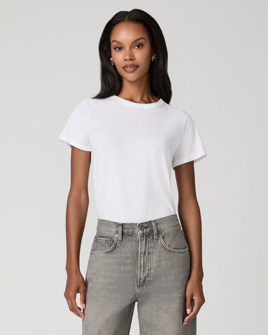 A woman standing in a white ribbed crew-neck tee and high-rise gray jeans, hands relaxed at her sides.
