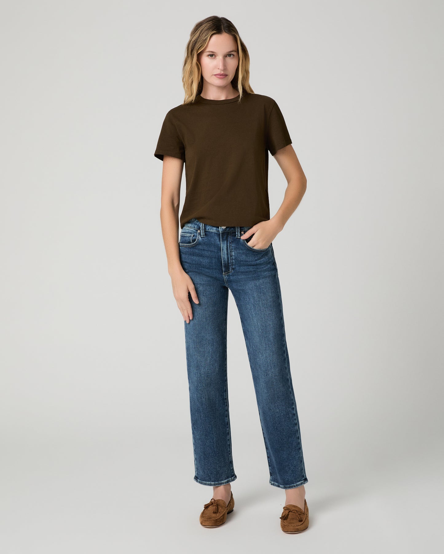 Women wearing green tee and blue jeans paired with chestnut flats against a white background