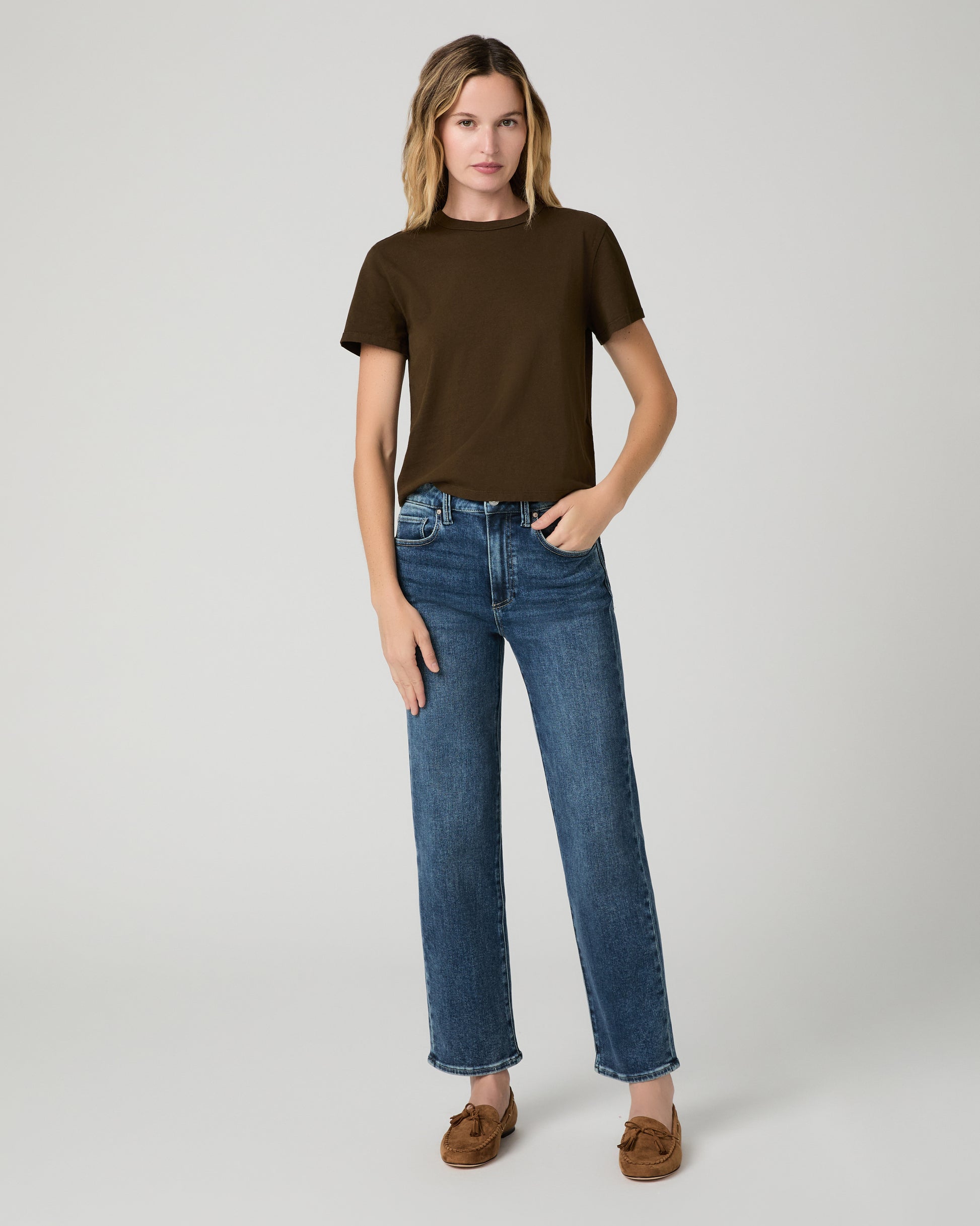 Women wearing green tee and blue jeans paired with chestnut flats against a white background