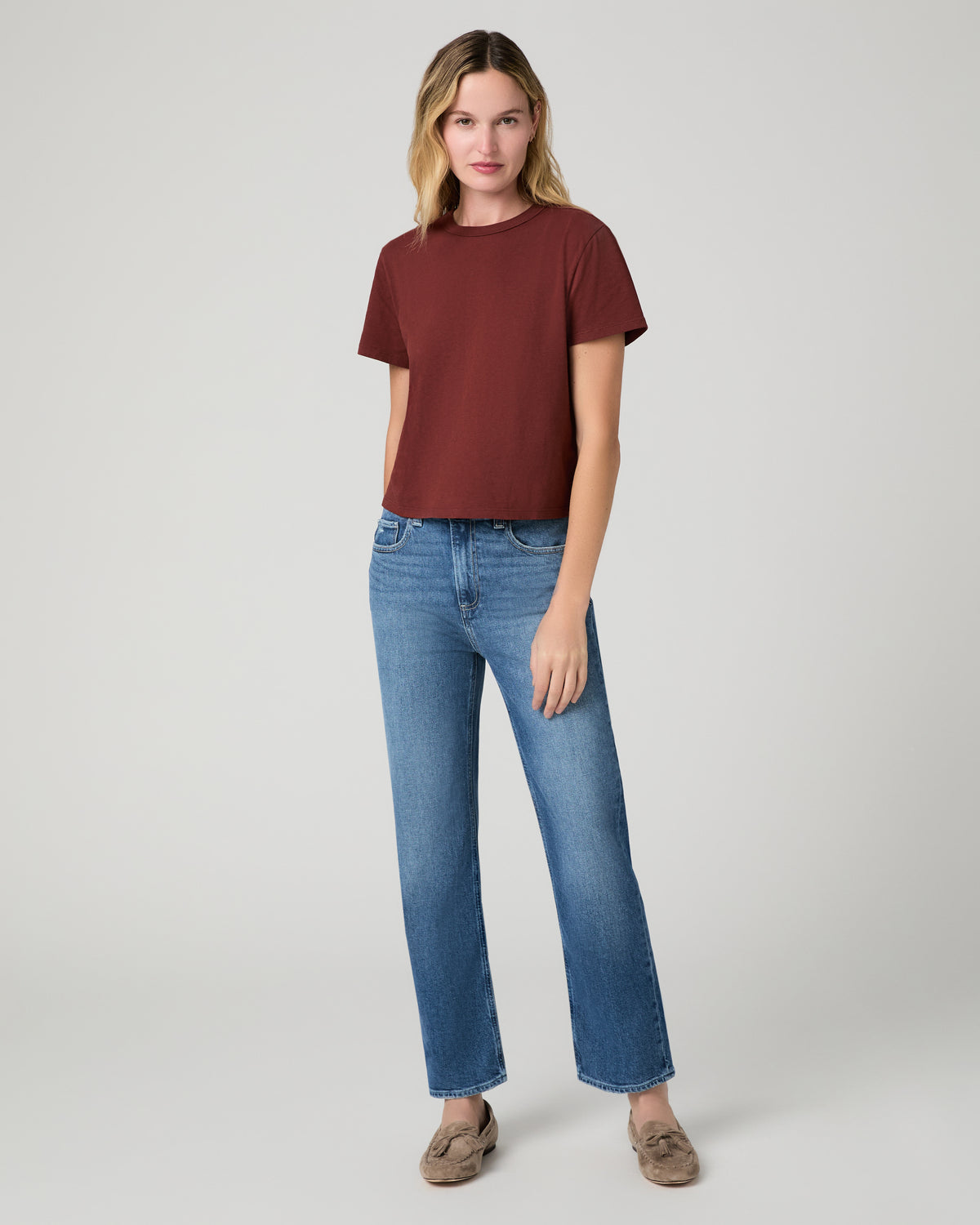 Women wearing red tee and blue jeans paired with brown flats against a white background